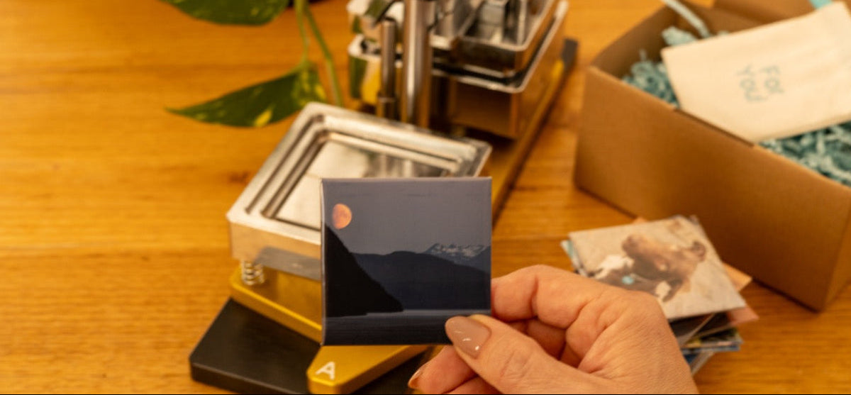 Person holding a small photo print next to photo printing equipment on a wooden table.